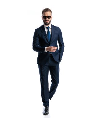 Donanma mavisi takım elbiseli mutlu, olgun bir adam gülümsüyor ve beyaz arka planda el ele yürüyor.