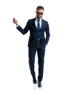 Güneş gözlüklü seksi, zarif adam parmaklarını sağa sola şıklatıyor ve beyaz arka planda yürüyor.