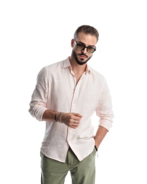 Güneş gözlüklü seksi genç adam beyaz arka planda el ele poz veriyor.