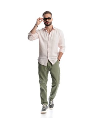 Güneş gözlüğü takarken ve beyaz arka planda gülümserken el ele yürüyen sıradan bir genç adam.