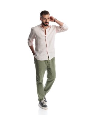 Kafası karışmış genç bir adam beyaz arka planda el ele yürürken kafasını kaşıyor.