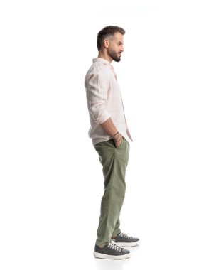 Beyaz arka planda elleri ceplerinde sırada bekleyen mutlu genç adamın yan görüntüsü