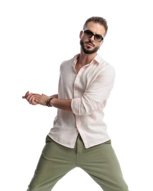 Güneş gözlüklü, kendine güvenen, avuç içi ovalayan ve beyaz arka planda poz veren havalı adam.