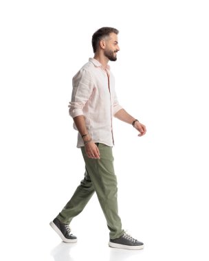 Yandan bakan, gülümseyen ve beyaz arka planda yürüyen mutlu sıradan bir adamın yan görüntüsü.