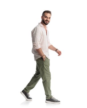 Cebinde el ele yürüyen ve beyaz arka planda gülümseyen mutlu genç adamın yan görüntüsü.