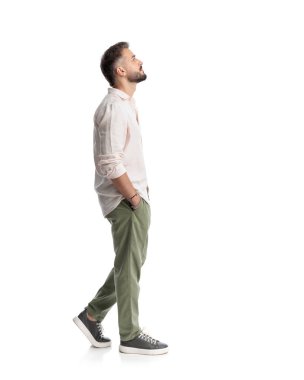 Düşünceli genç adam ellerini cebine sokup beyaz arka planda öne doğru adımını atıyor.