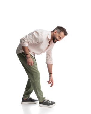 Beyaz arka planda yürürken yerden bir şey kapmak için gülümseyen ve eğilen mutlu sıradan bir adamın yan görüntüsü