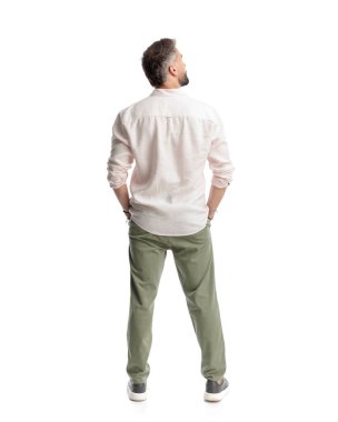 Genç, sıradan bir adam ceplerinde el ele tutuşuyor ve beyaz arka planda dikilirken yan tarafa bakıyor.