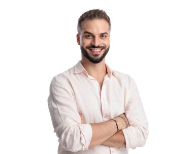 Yakışıklı, mutlu, sakallı, ileriye bakan, kollarını kavuşturup beyaz arka planda gülümseyen bir adam.