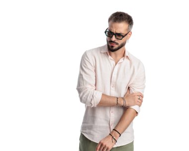 Güneş gözlüklü seksi adamın portresi aşağı bakıyor ve beyaz arka planda gömlek ayarlıyor.