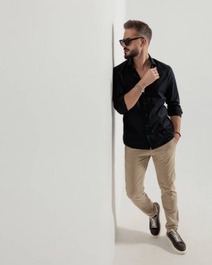 Güneş gözlüklü kibirli genç adam elini cebine atarak duvara bakıyor. 