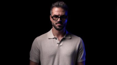 Siyah arkaplan önünde güneş gözlüklerini ayarlayan sıradan bir gencin videosu.