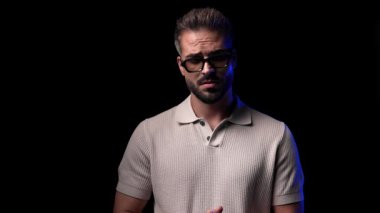 Güneş gözlüklü, sessiz hareketler yapan ve siyah arkaplan önünde yürüyüp giden seksi genç adamın video projesini.