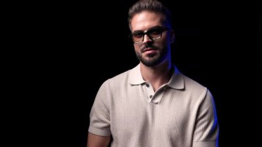 Polo tişörtlü sakallı genç adam yan bakıyor, yürüyor, ellere dokunuyor ve karanlıkta arka planda saklanıyor.