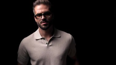 Güneş gözlüklü sıradan bir genç adam yan tarafa bakıyor ve elleriyle alnına vuruyor, gülüyor ve siyah arka planda eğleniyor.