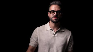 Polo tişörtlü seksi adam güneş gözlüğünü çıkarıyor, kollarını kavuşturuyor ve siyah arka planın önüne bakıyor.