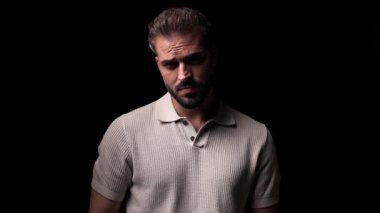 Yakışıklı sakallı adam güneş gözlüğü takıyor, önüne bakıyor ve siyah arka planın önünde duruyor.