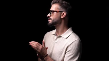 Polo tişörtlü, güneş gözlüklü, avuç içi ovalayan ve siyah arka planın önüne geçmek isteyen çekici bir moda adamı.