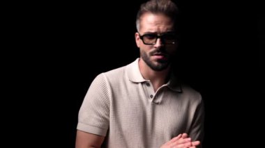 Güneş gözlüklü, yürüyen, avuçlarını ovuşturan, kendini kucaklayan ve siyah arka planda yer alan seksi bir adam.