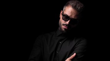 Dramatik havalı adam fener ışığında poz veriyor, güneş gözlüğü takıyor, kendine dokunuyor ve siyah arkaplanın önüne bakıyor.