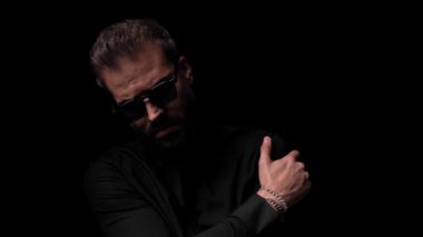 Kendini kucaklayan ve siyah arka planda havalı bir şekilde ağzına dokunan seksi bir adamın video kasedi.