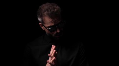 Güneş gözlüklü yakışıklı adam avuçlarını ovalıyor ve yan tarafa bakarken özgüvenle poz veriyor ve siyah arka planda yanıp sönen ışıkları dört gözle bekliyor.