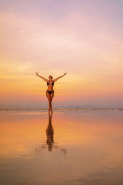 Gün batımında sahilde genç ve zinde bir kadının silueti. 