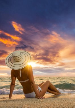 Gün batımında sahilde poz veren mayo giymiş bir kadın.