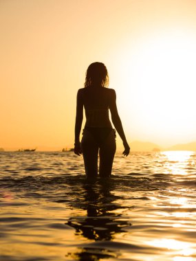 Gün batımında denizde yürüyen genç bir kadın.