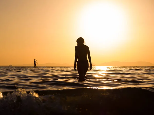 Jeune femme marchant dans la mer au coucher du soleil — Photo