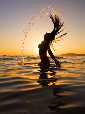 Gün batımında denizde yürüyen genç bir kadının silueti.