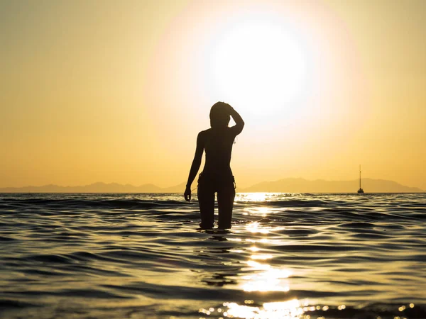 日落时在海里散步的年轻女子 — 图库照片