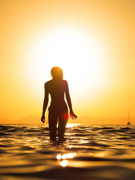 Ung kvinna promenader i havet vid solnedgången — Stockfoto