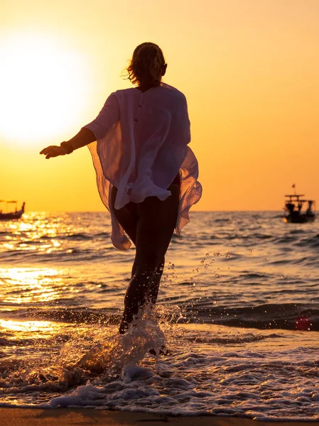 Jeune femme marchant dans la mer au coucher du soleil — Photo