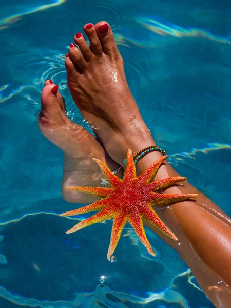 Pernas de mulher com estrela do mar na piscina — Fotografia de Stock