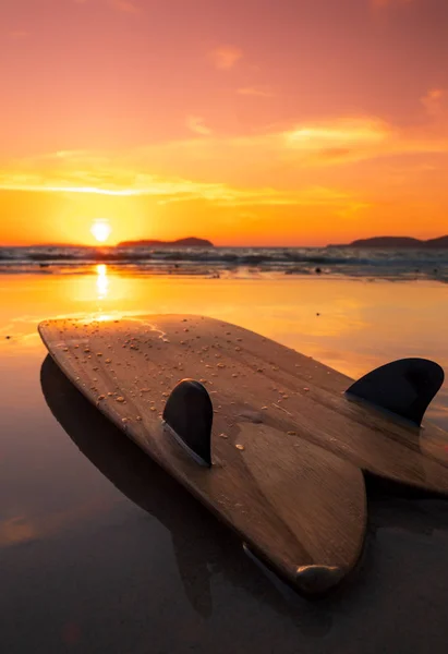 Tabla de surf en la playa en la orilla del mar al atardecer —  Fotos de Stock