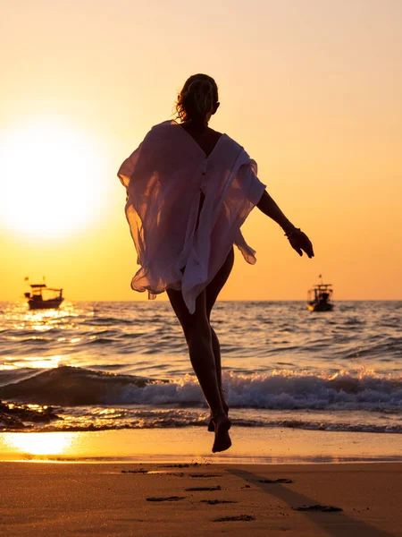 Jeune femme marchant dans la mer au coucher du soleil — Photo