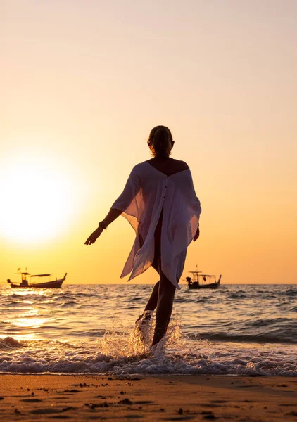 Jeune femme marchant dans la mer au coucher du soleil — Photo