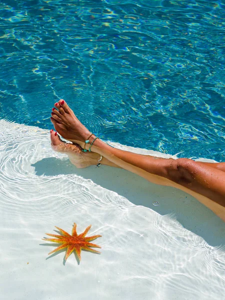 Jambes de femme avec étoile de mer à la piscine — Photo