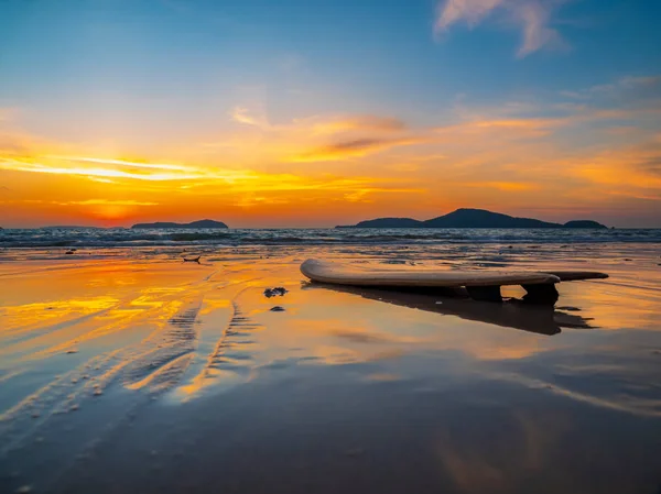 Tabla de surf en la playa en la orilla del mar al atardecer — Foto de Stock