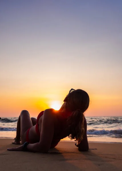 Vrouw zittend op het strand bij zonsondergang — Stockfoto