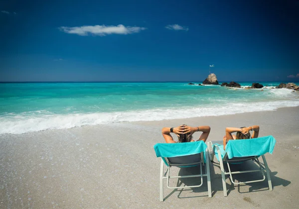Casal em espreguiçadeiras relaxando na praia em Lefkada — Fotografia de Stock