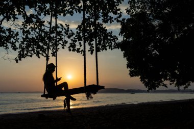 Gün batımında sahilde sallanan bir kadın.