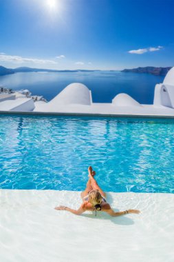 Havuzda dinlenen bir kadın ve Santorini Yunanistan manzarasına bakıyor