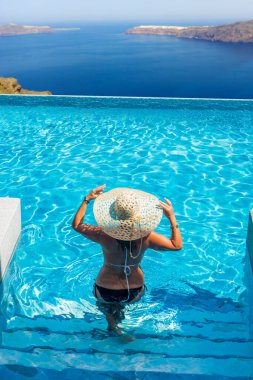 Havuzda dinlenen bir kadın ve Santorini Yunanistan manzarasına bakıyor