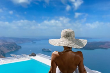 Yunanistan 'ın Santorini adasındaki yüzme havuzunda, Caldera manzaralı lüks bir tatil yapan bir kadın.