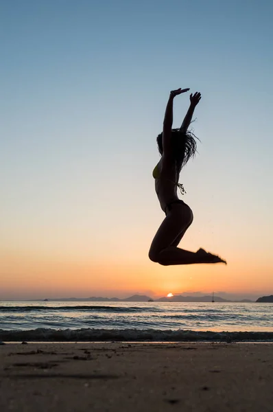Woman in swiming suit jumping on the beach at sunset