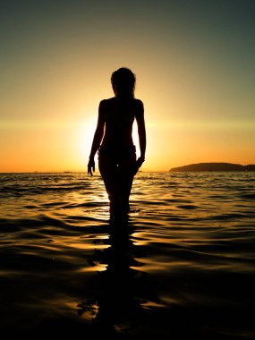 Gün batımında sahilde poz veren mayo giymiş bir kadın.