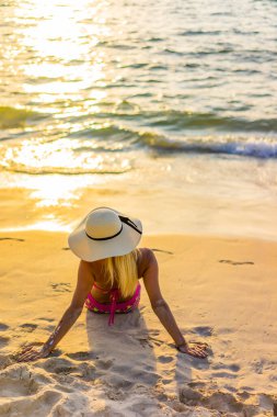 Gün batımında sahilde poz veren mayo giymiş bir kadın.
