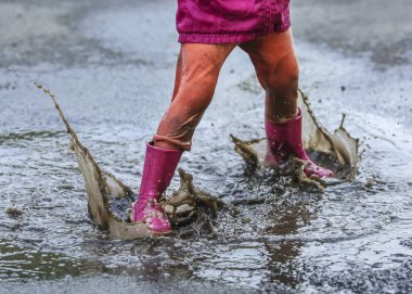 Playful child outdoor jump into puddle in boot after rain clipart